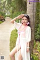 A woman in a pink and white dress leaning against a palm tree.