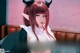 A woman with red hair and horns sitting on a bed.