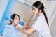 A woman in a white lab coat is getting her teeth examined by a nurse.